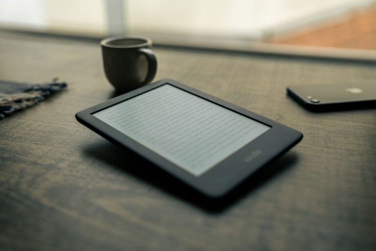 E-reader displaying text on a wooden table, beside a coffee cup and smartphone, illustrating a cozy reading environment.